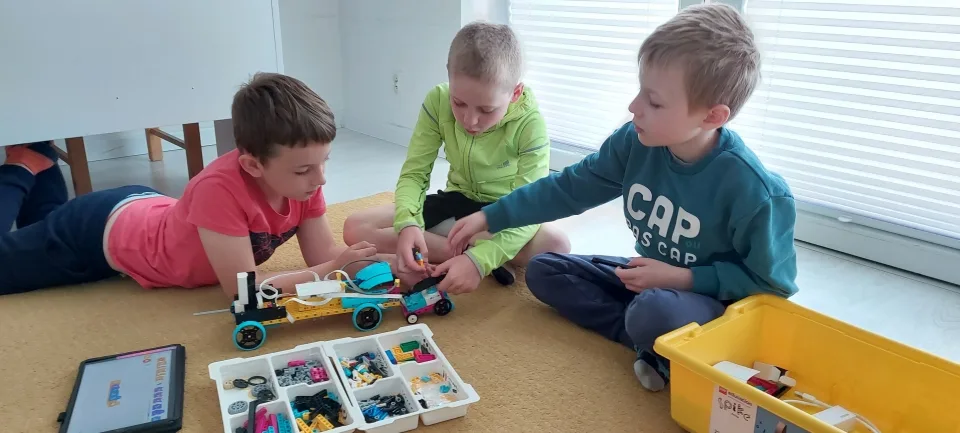 Trójka dzieci pracuje zespołowo nad projektem LEGO na warsztatach STEAM FA-BRYKA